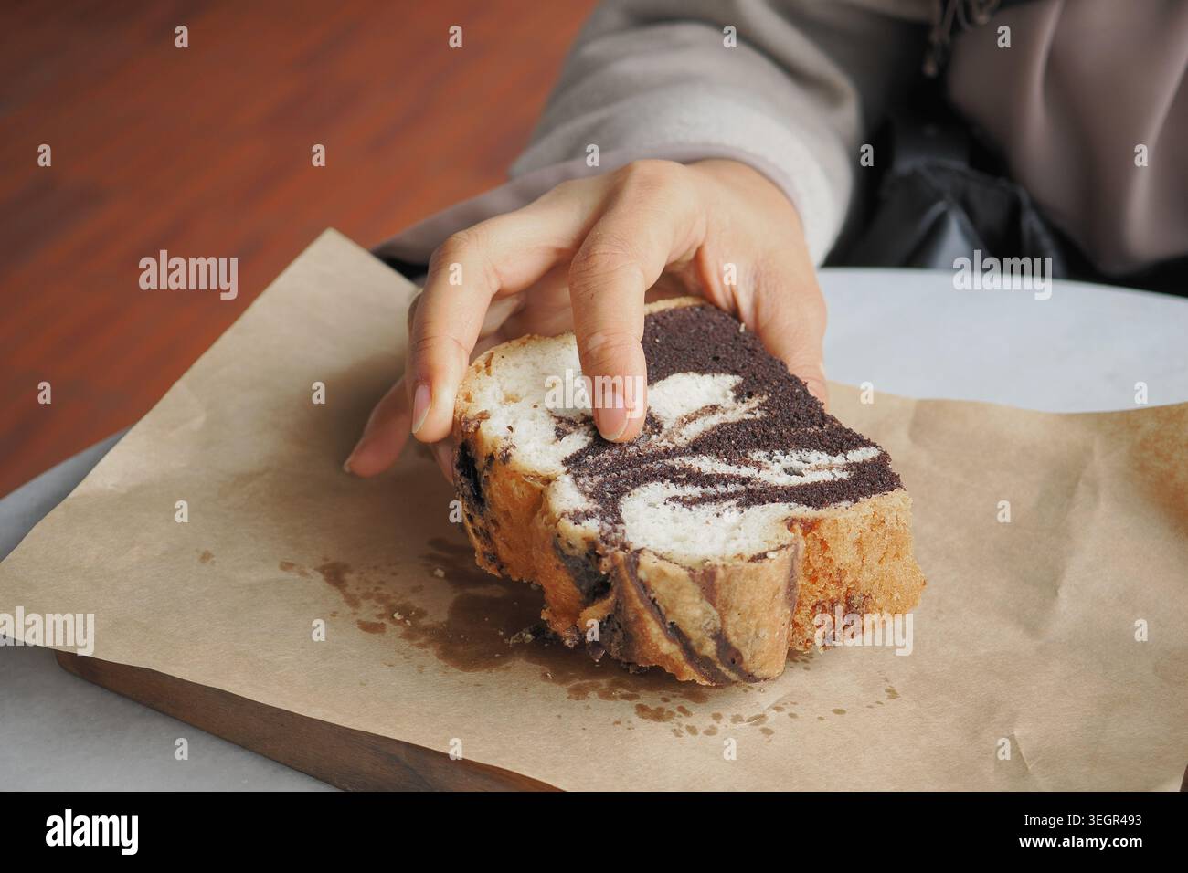 La mano raggiunge una fetta di pane marmorizzato sulla carta Foto Stock