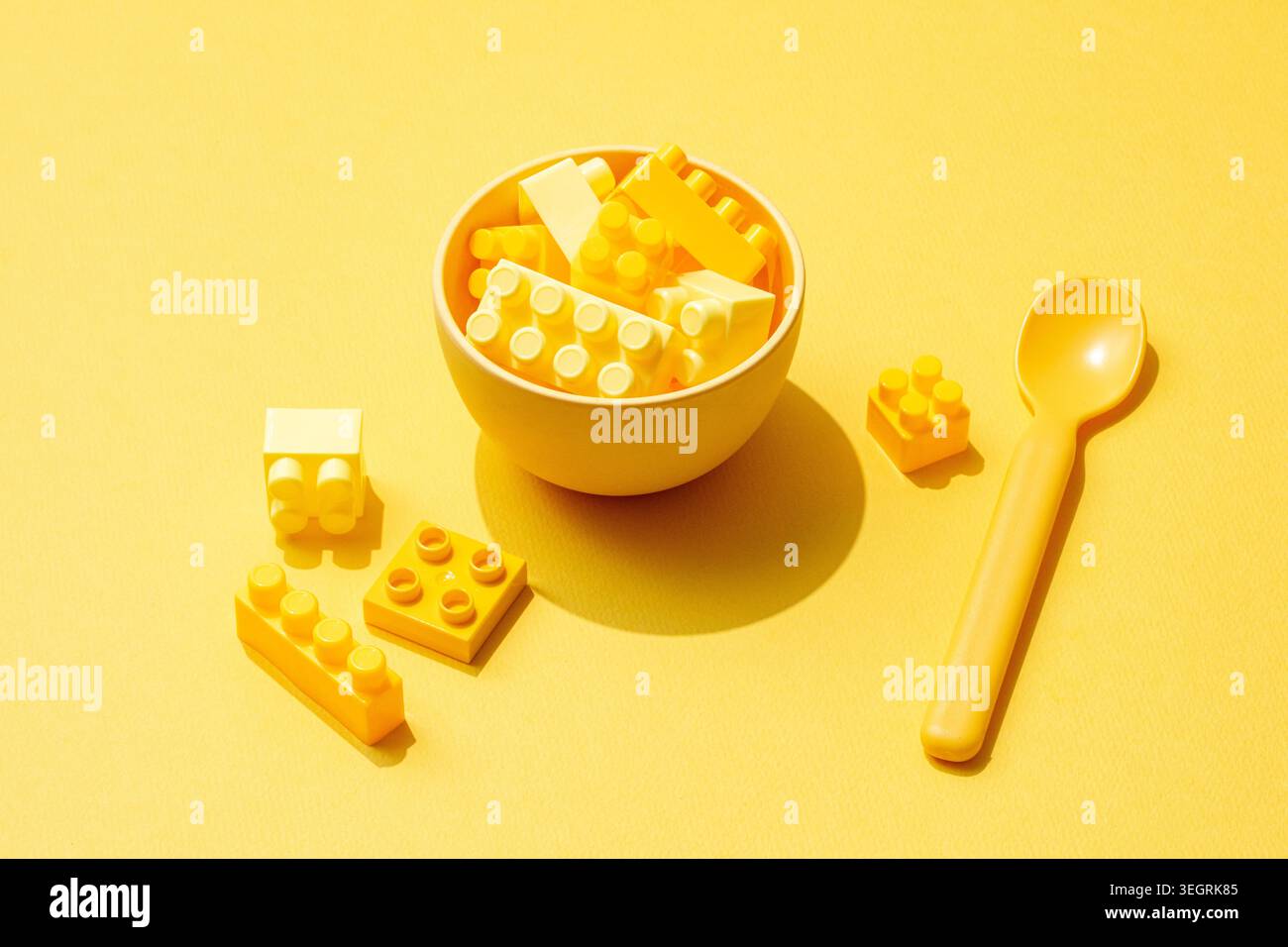 Una ciotola di mattoncini LEGO colorati viene utilizzata come accessorio creativo per il cibo su un tavolo giallo brillante. Foto Stock