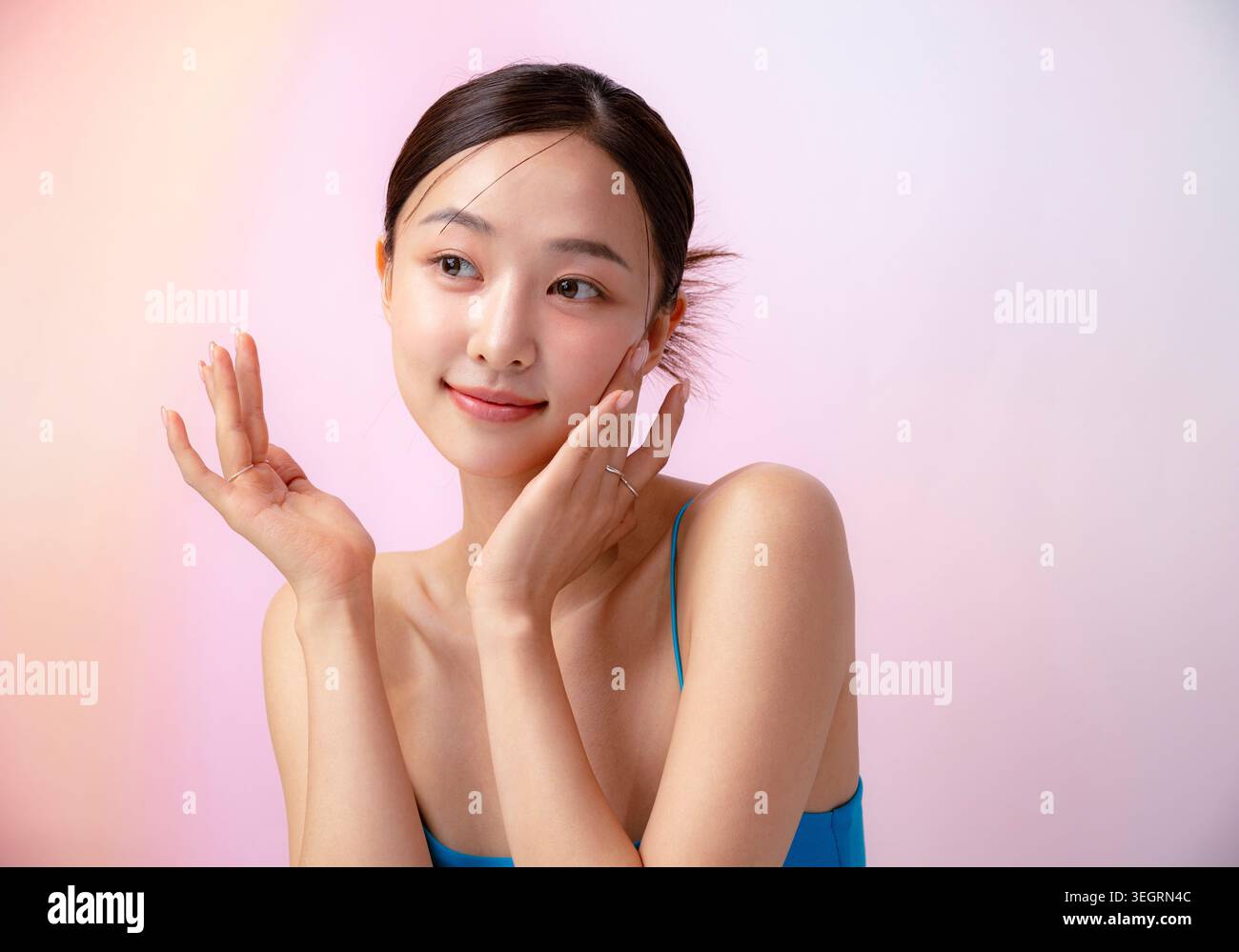 Una giovane donna asiatica con le mani sulle guance, sorridente e che guarda direttamente la fotocamera. Foto Stock