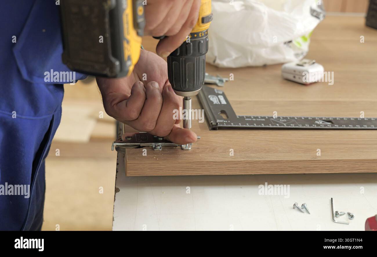 Lavoratore che utilizza un trapano elettrico per fissare le viti in un pannello di legno, mobili da costruzione o armadi in un ambiente di officina, concentrandosi sui costrutti Foto Stock