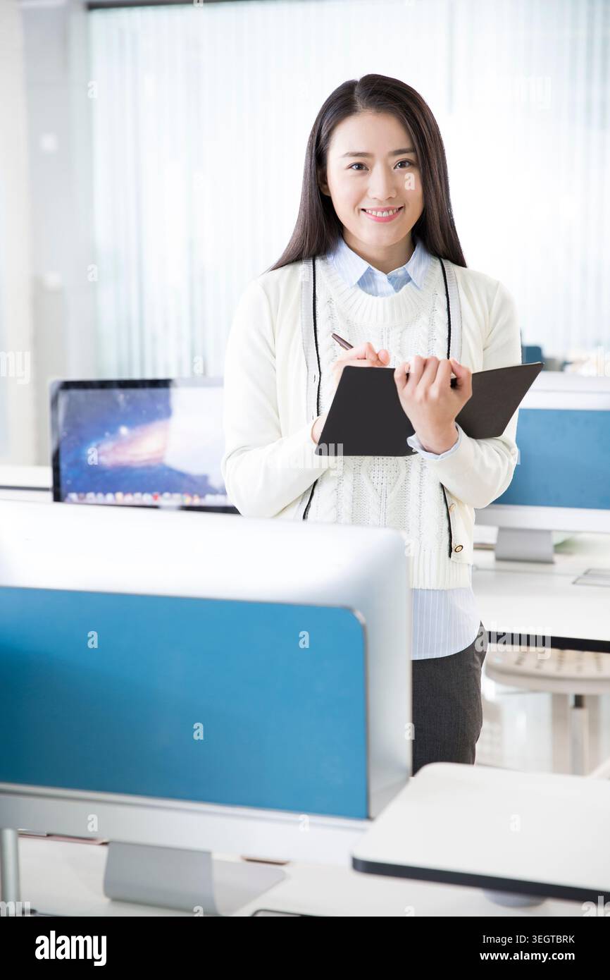 Una giovane donna in un ufficio moderno tiene un appunti e sorride mentre lavora. Foto Stock