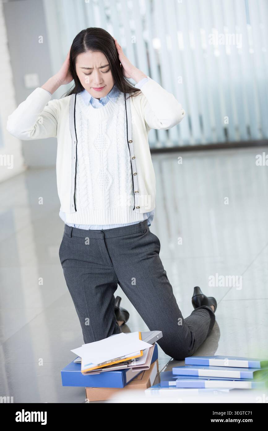 Una lavoratrice d'ufficio stressata si inginocchia in una scrivania disordinata, tenendo la testa tra le mani. Foto Stock