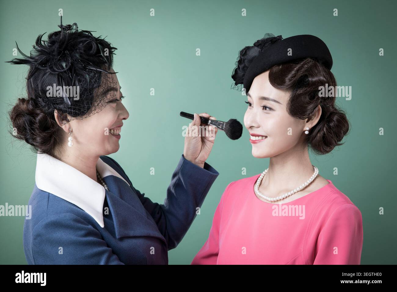 Una donna con un outfit in stile anni '1940 applica il trucco a una giovane donna con un abito in stile anni '1940 in un ambiente studio. Foto Stock