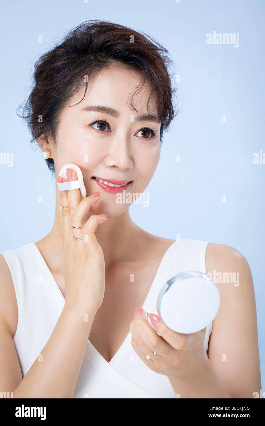 Una donna sorride mentre applica le fondamenta al viso davanti a uno specchio. Foto Stock
