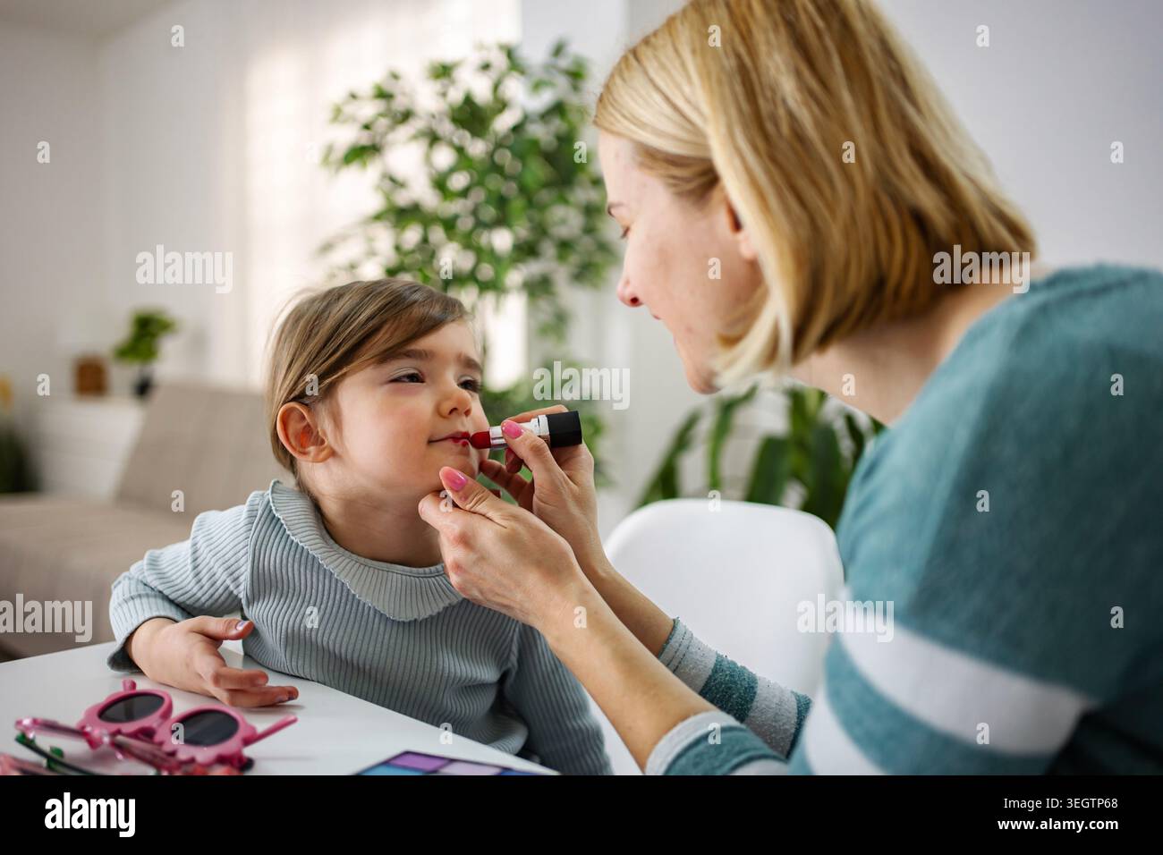 Madre che applica il rossetto alla figlia che impara il trucco a casa Foto Stock