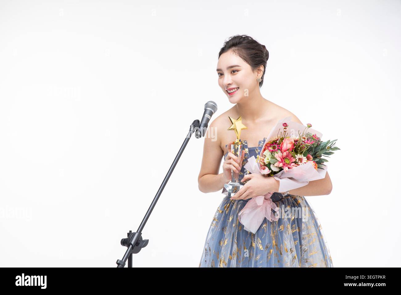 Una giovane donna tiene un trofeo e sorride mentre si rivolge al pubblico da un microfono. Foto Stock
