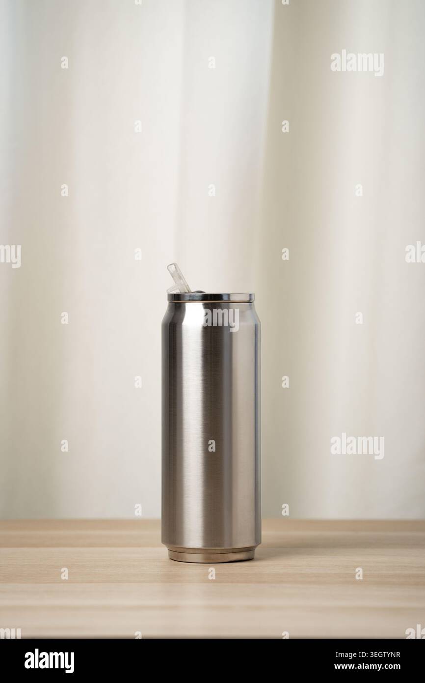 Bicchierino in acciaio inox con cannuccia trasparente su un tavolo in legno, dal design minimalista e moderno. Contenitore isolato portatile per bevande fredde, riutilizzabile ed eco-f Foto Stock