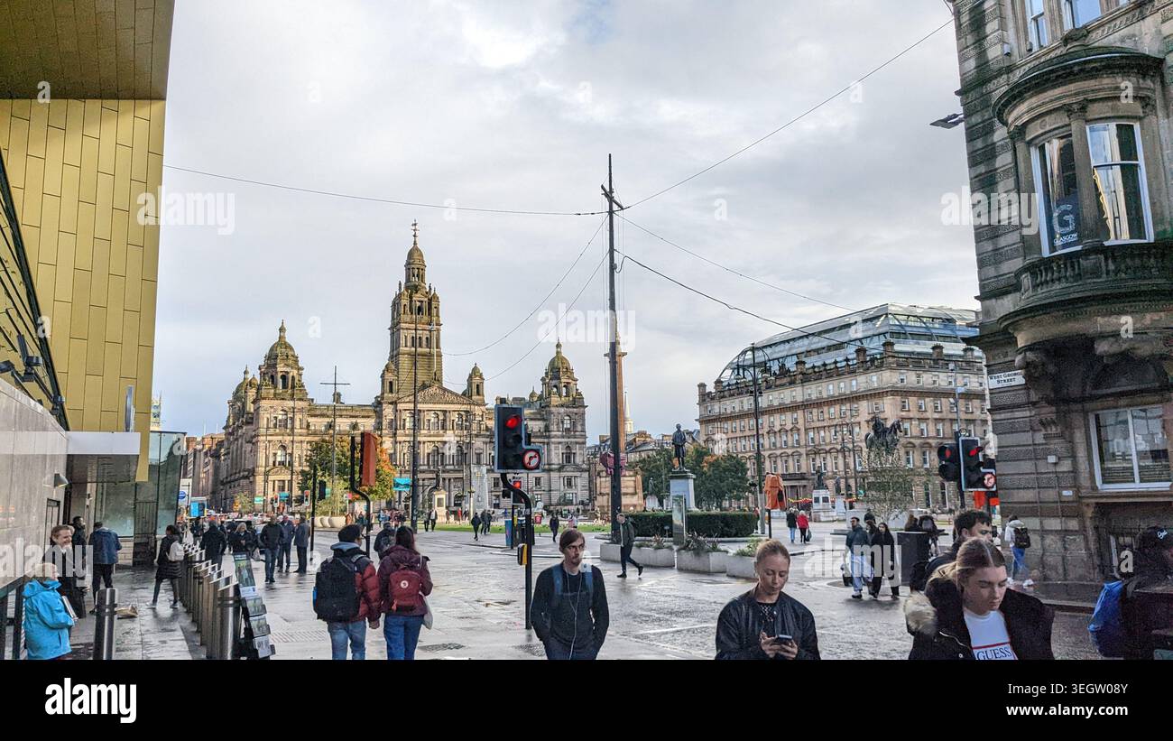 George Square nel centro di Glasgow, con pedoni che camminano sul pavimento bagnato di fronte alle storiche camere della città di Glasgow e all'architetto circostante - Immagine stock catturata con smartphone