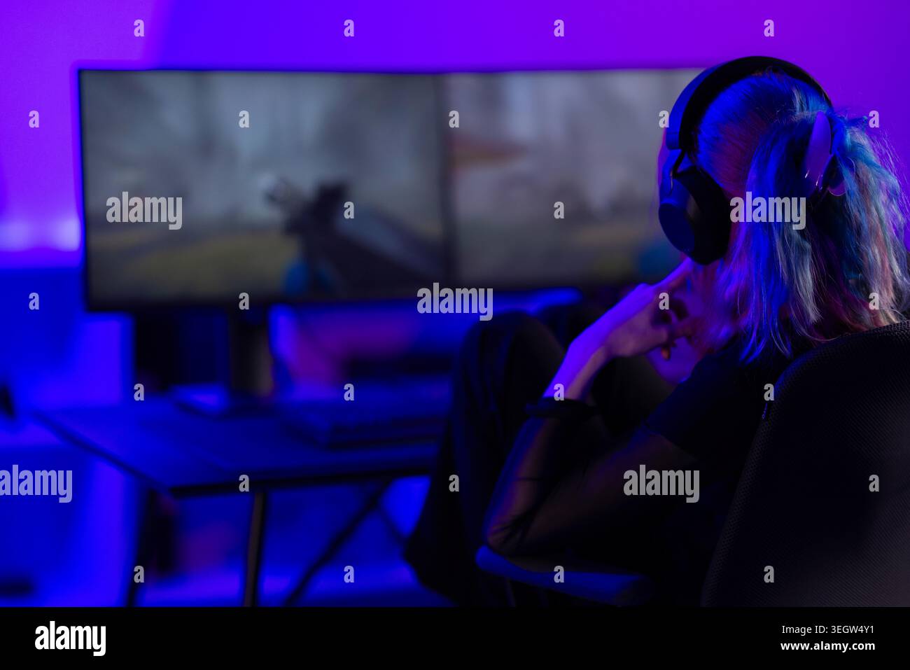Giovane videogamer femminile che si concentra sul gioco d'azione in una configurazione di gioco illuminata al neon Foto Stock