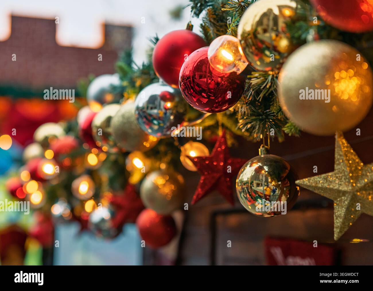 Gli ornamenti natalizi rossi, dorati e argentati sono appesi alla ghirlanda verde, illuminati da luci calde. Foto Stock
