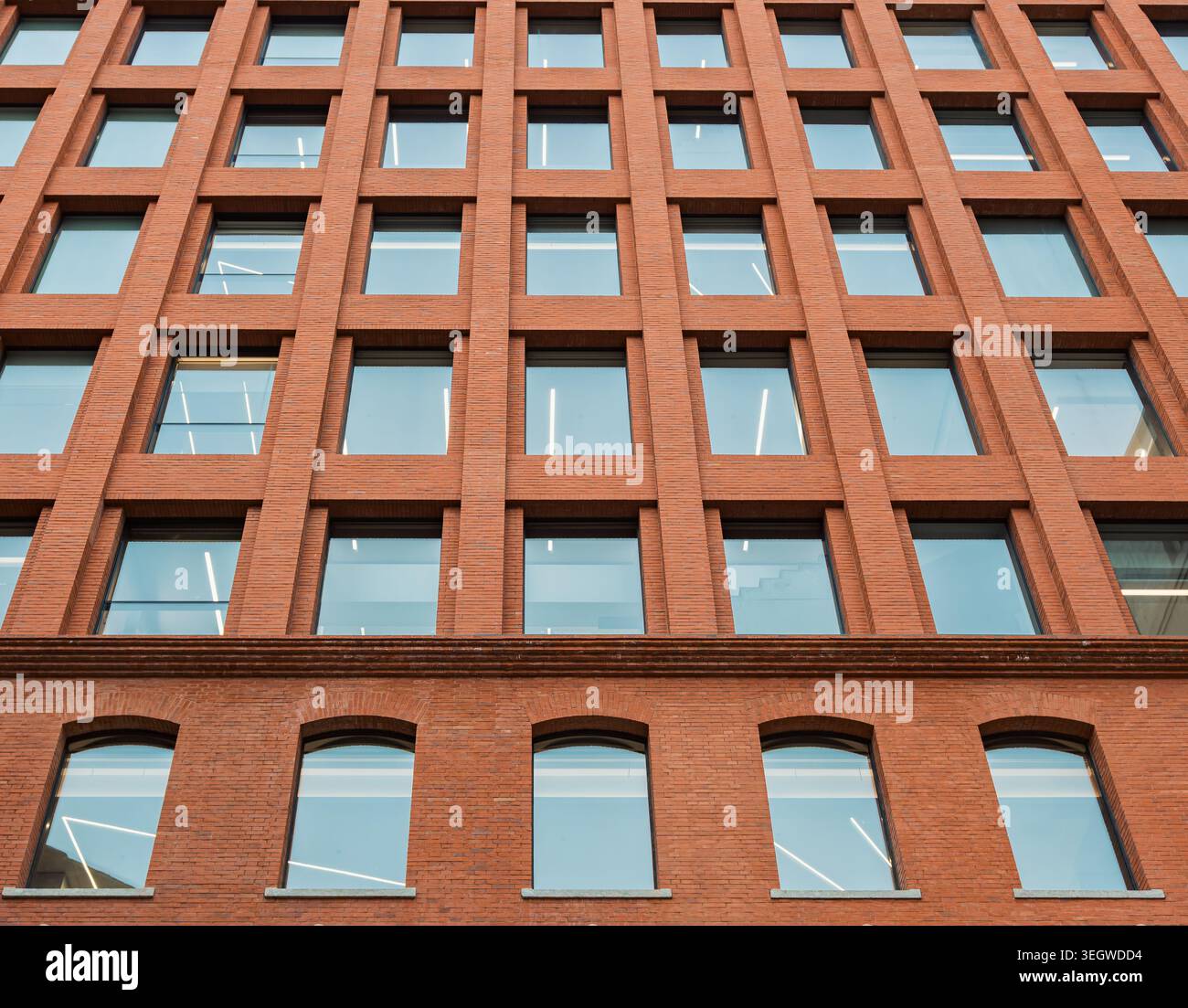 Vista ascendente di un edificio contemporaneo in mattoni caratterizzato da una griglia di molte finestre quadrate e finestre ad arco su un livello inferiore Foto Stock