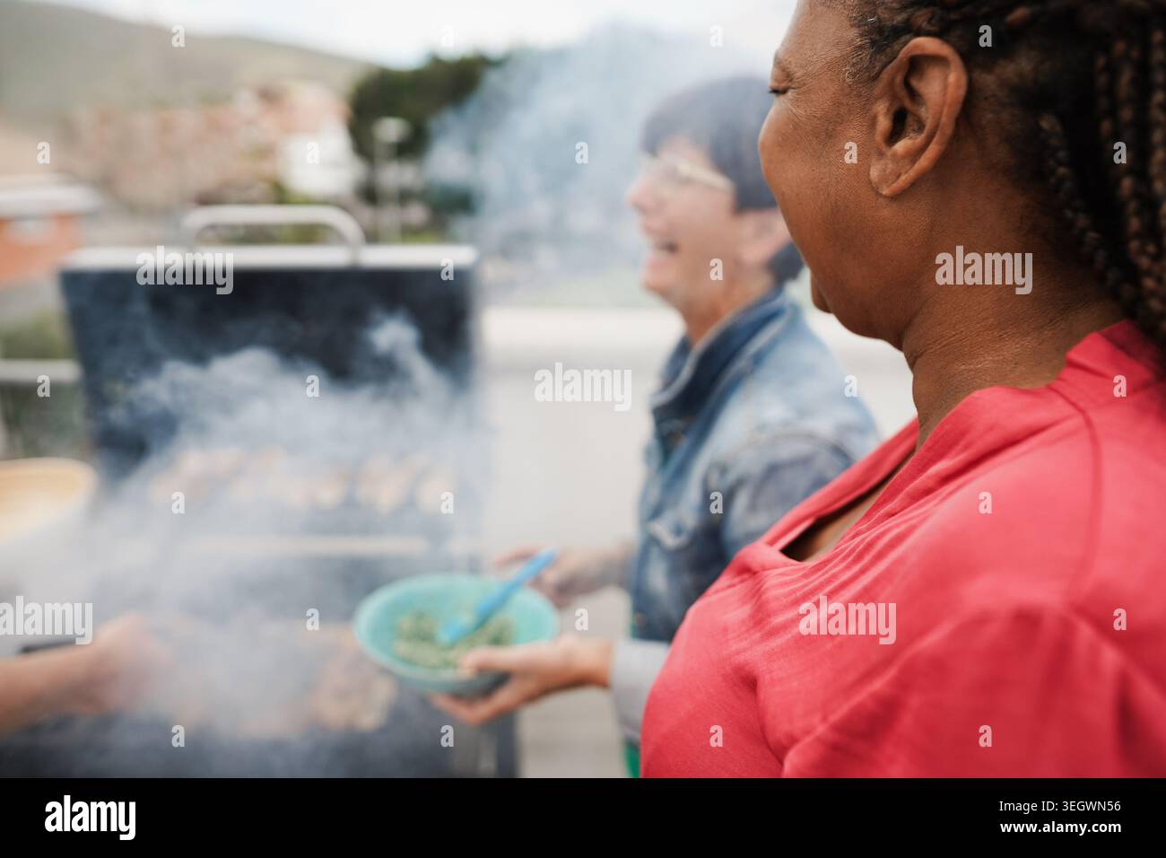 Amici anziani multirazziali che fanno barbecue sul tetto di casa - concetto di stile di vita per persone anziane, estive e mature - attenzione principale all'orecchio delle donne africane Foto Stock