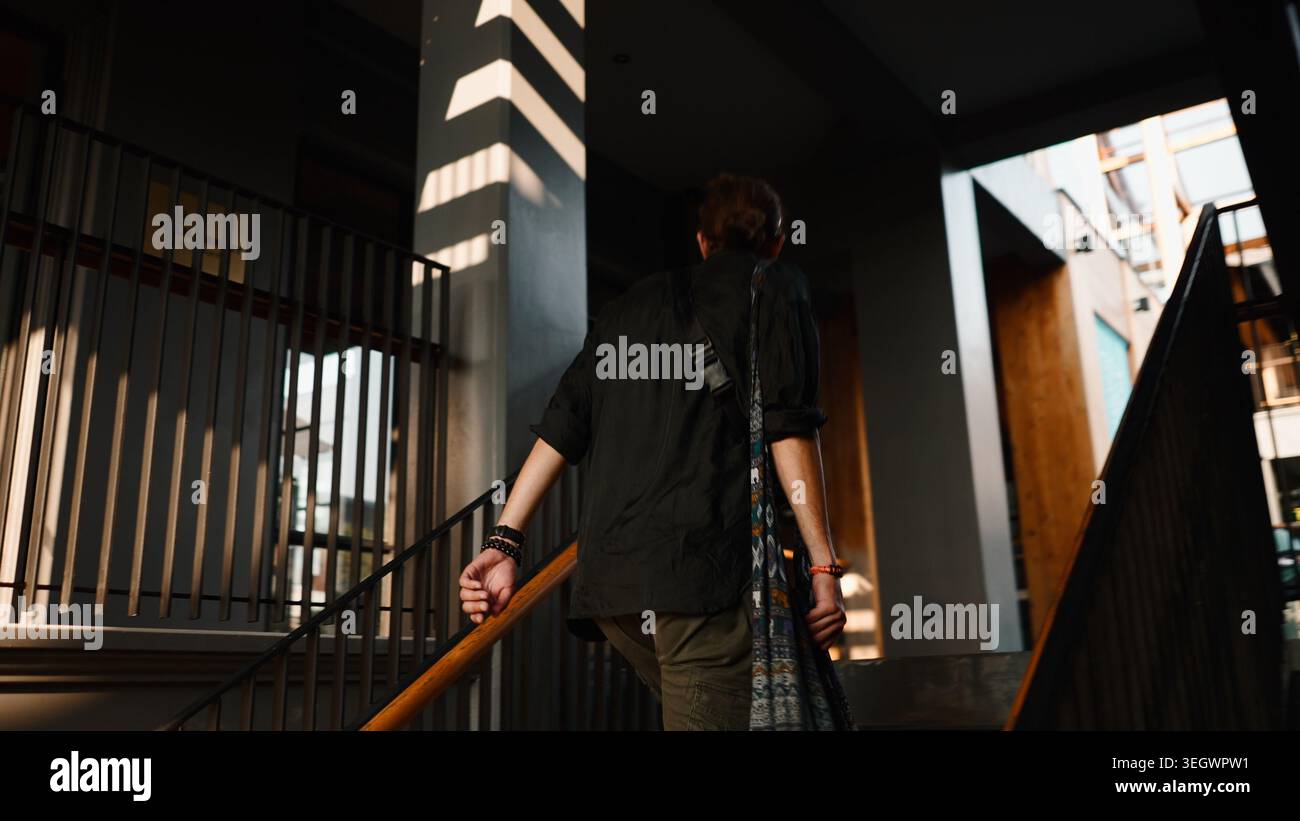 Uomo che cammina al piano di sopra con una borsa, con motivi d'ombra a strisce che gettano la luce del sole Foto Stock