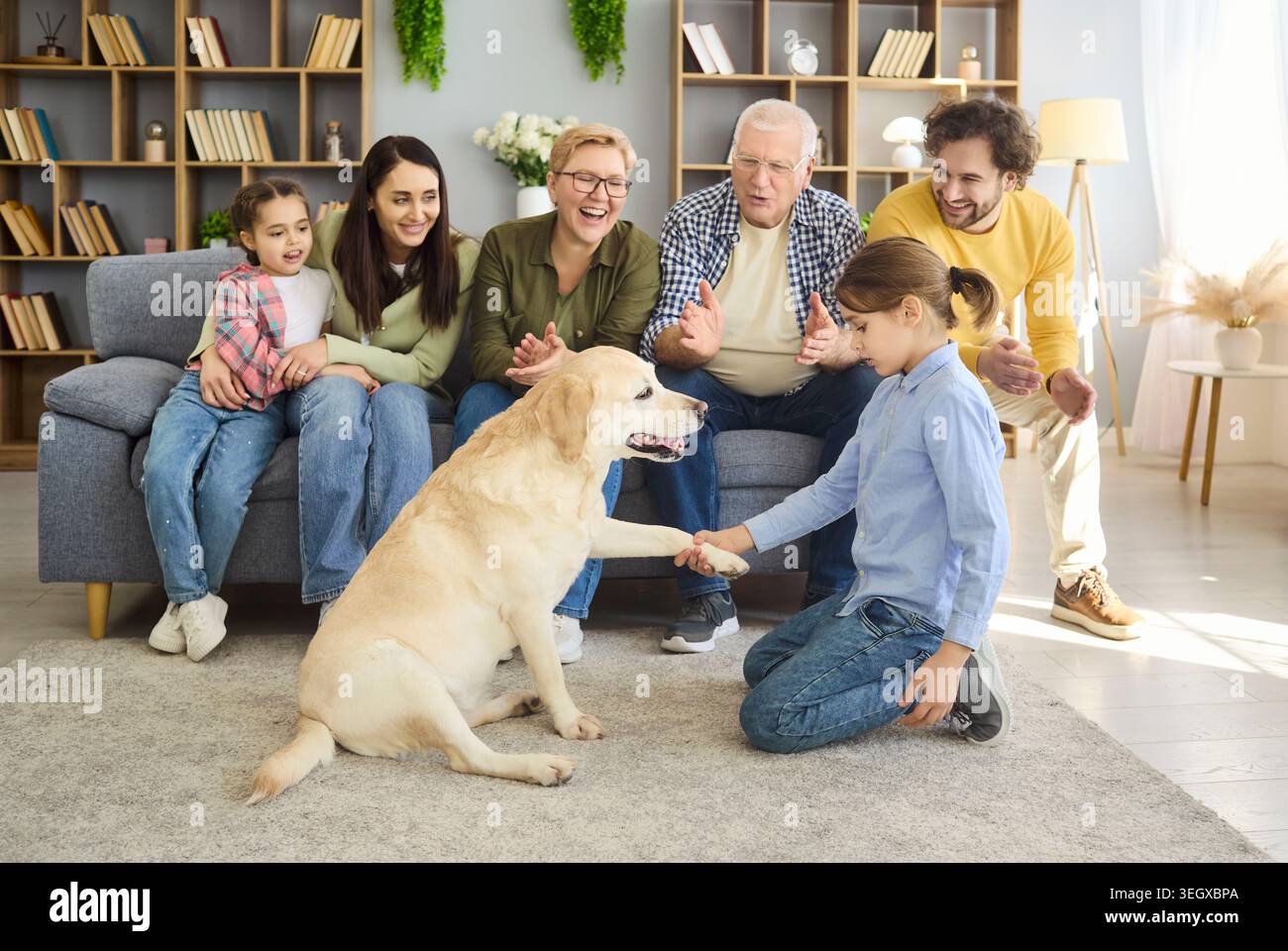 Felice famiglia multigenerazionale con labrador che gioca a casa, ragazza che trema zampa Foto Stock