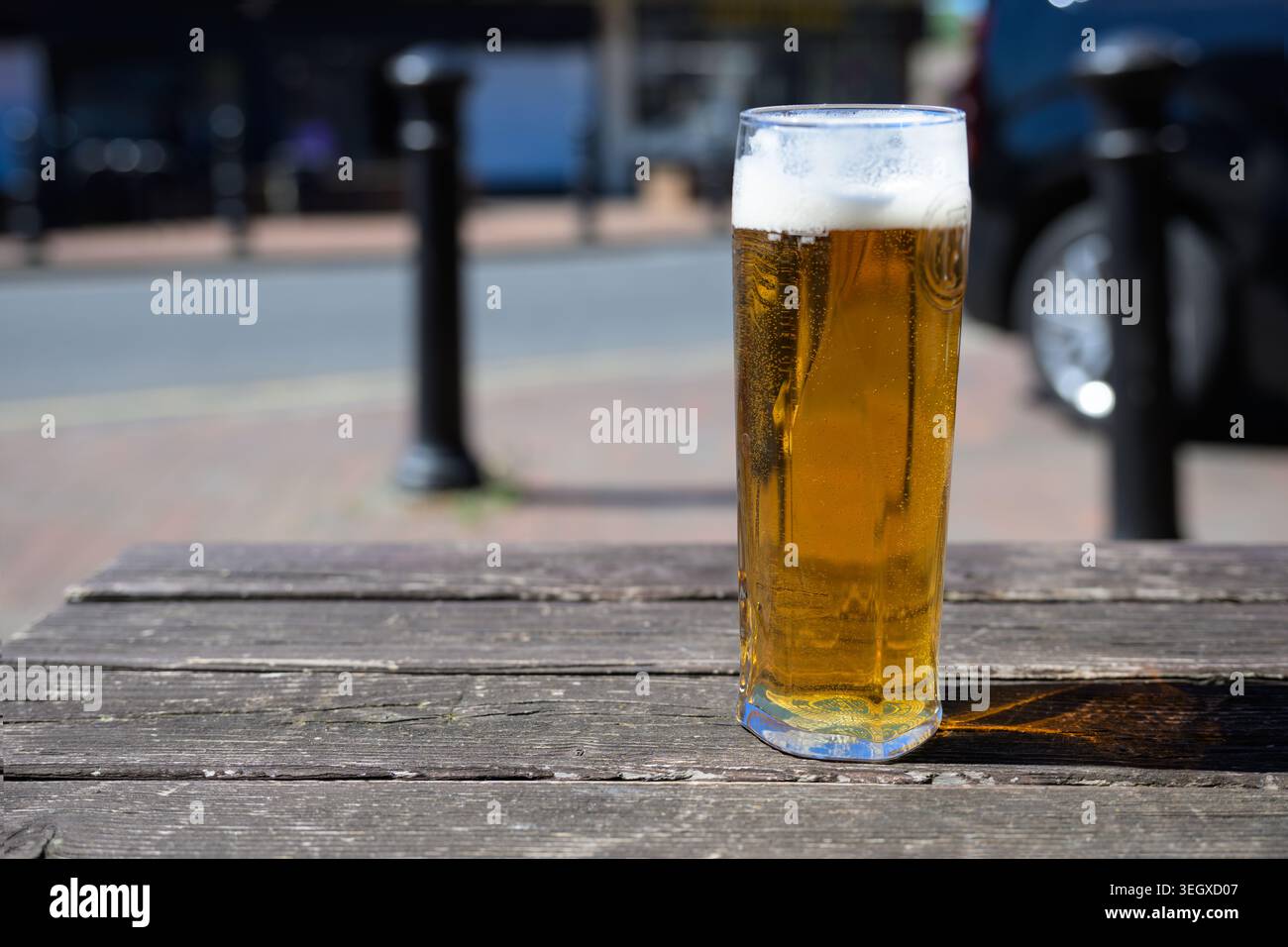 Rinfrescante pinta di lager su una panchina da pub all'aperto, in piena luce del sole e con un cielo azzurro, ideale per il tempo libero estivo e per i temi dello stile di vita dei pub. Foto Stock