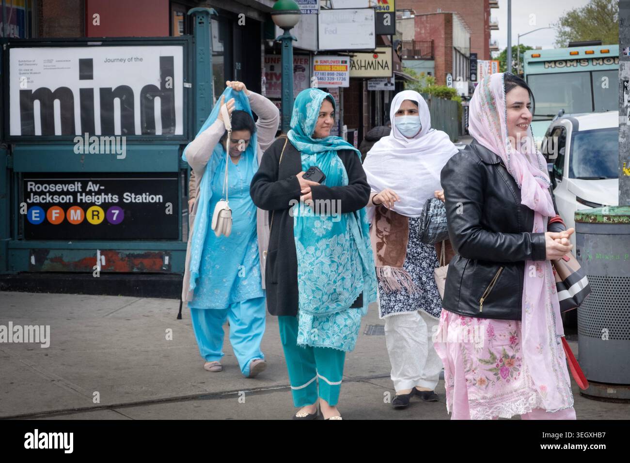 4 donne musulmane che attraversano una strada per dirigersi verso Diversity Plaza nel Queens con un grande cartello MENTALE dietro di loro. Foto Stock