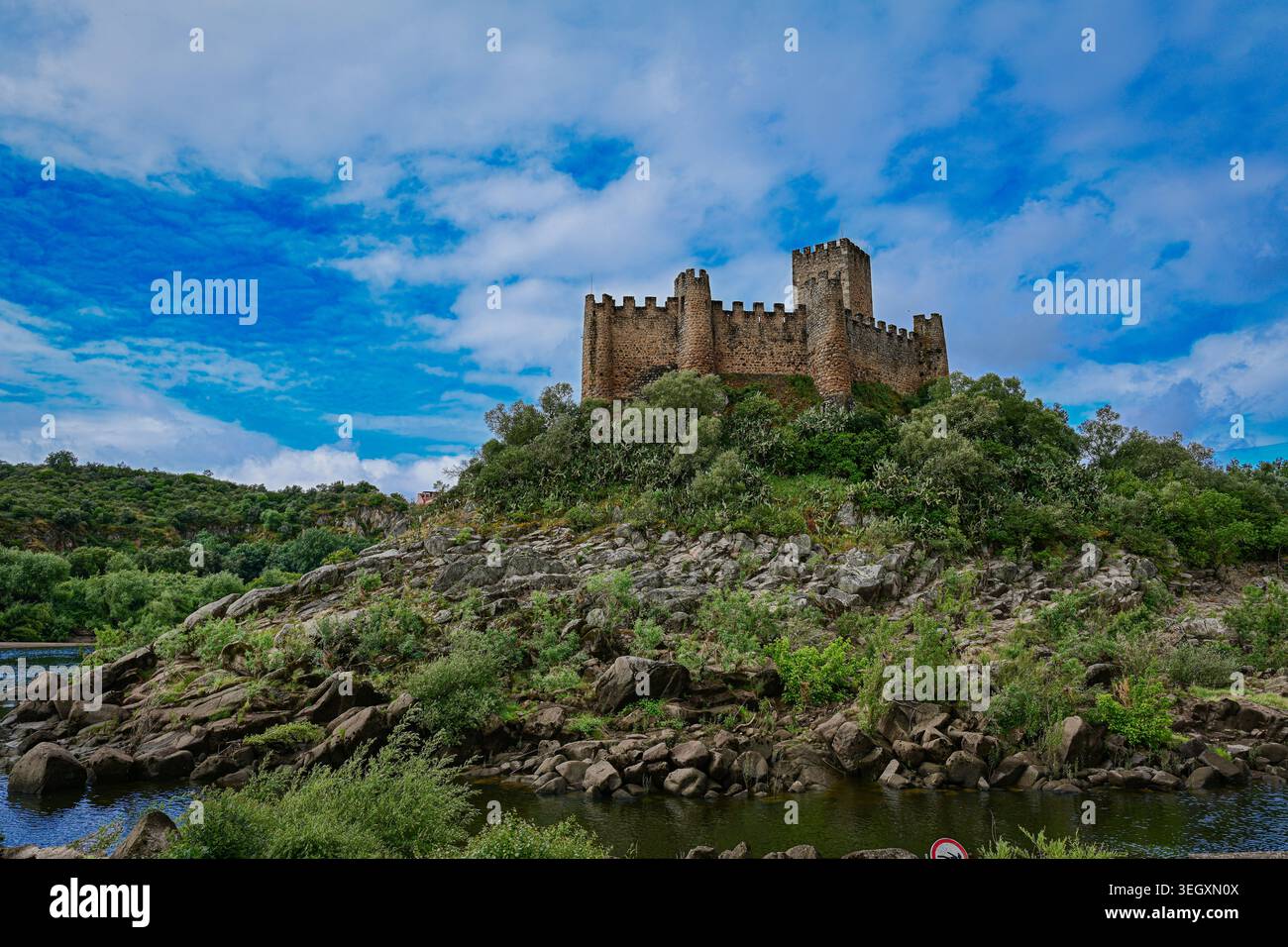 Suggestivo castello medievale in pietra che sorge sopra un paesaggio roccioso lungo il fiume in Portogallo, sotto cieli e nuvole blu vibranti. Foto Stock