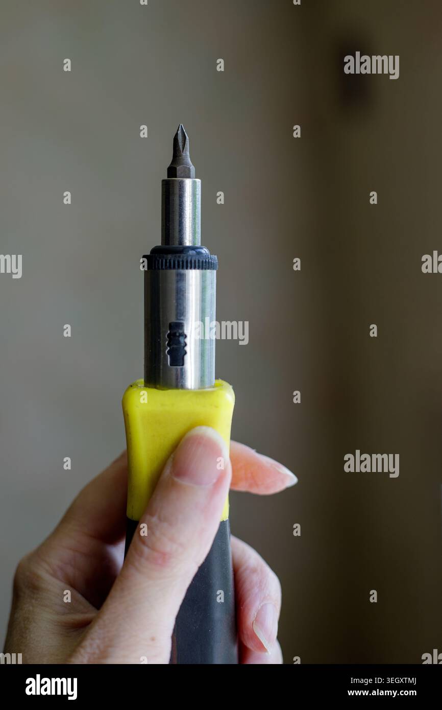 Operatore che afferra un cacciavite a punta intercambiabile. Attrezzatura tecnica per il serraggio dei dispositivi di fissaggio durante lavori di riparazione domestica o di manutenzione di appartamenti Foto Stock