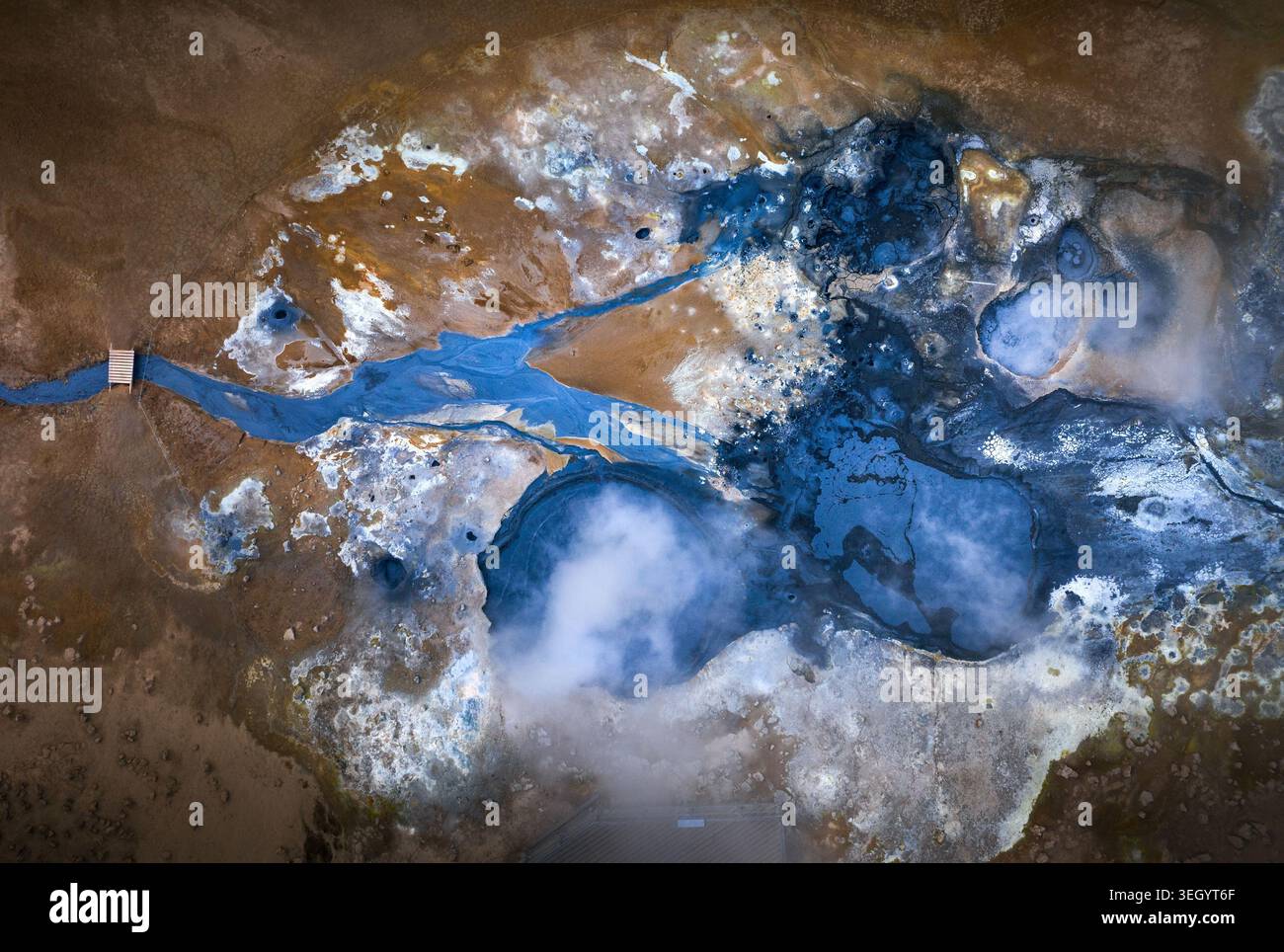 Vista aerea di un campo geotermico caratterizzato da piscine di fango blu vibranti, sfiati del vapore in aumento e terra arancione ricca di minerali attraverso il paesaggio vulcanico di Foto Stock