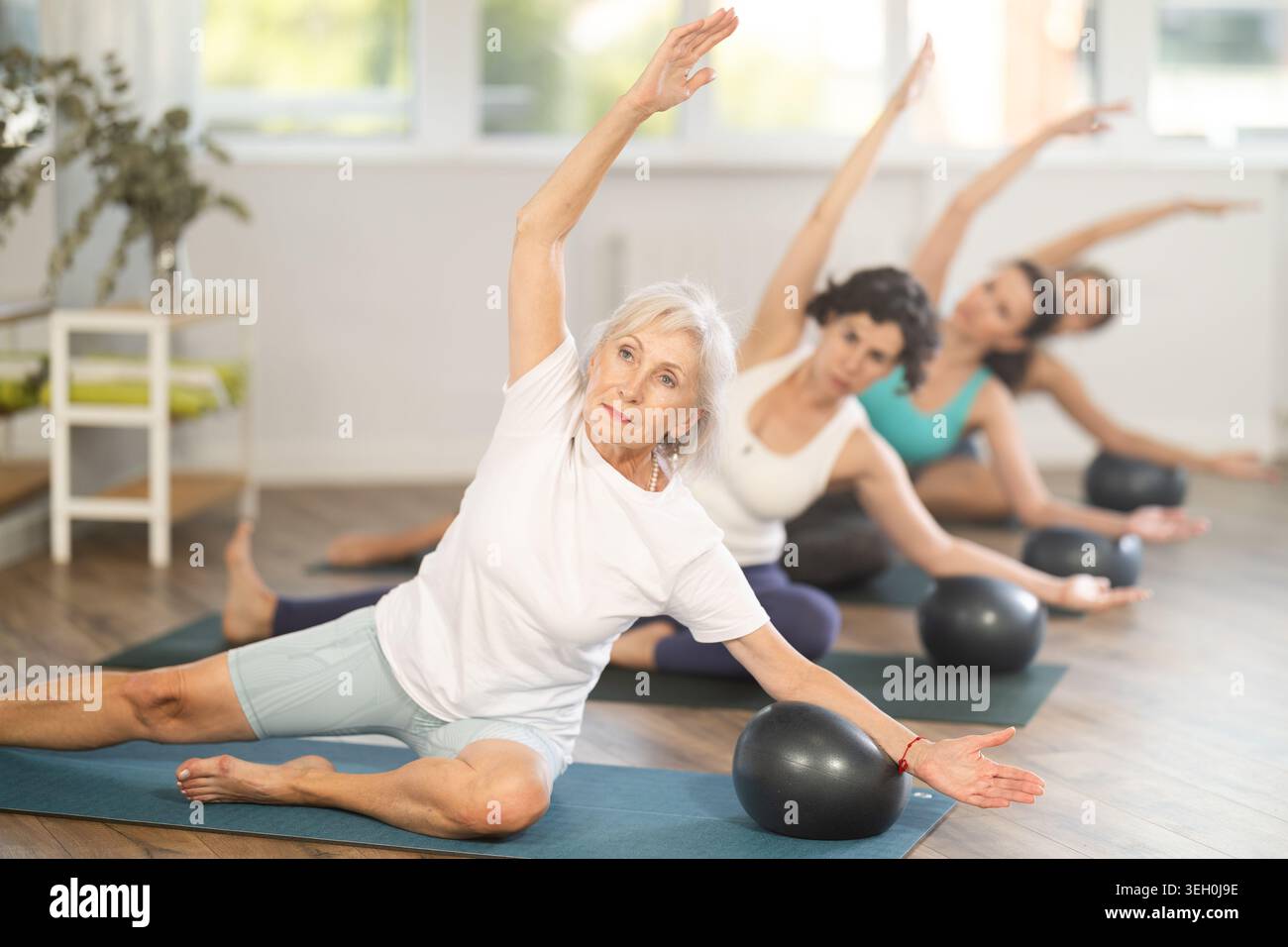 Donna anziana che fa Mermaid Stretch con Ball nel gruppo Pilates studio Foto Stock