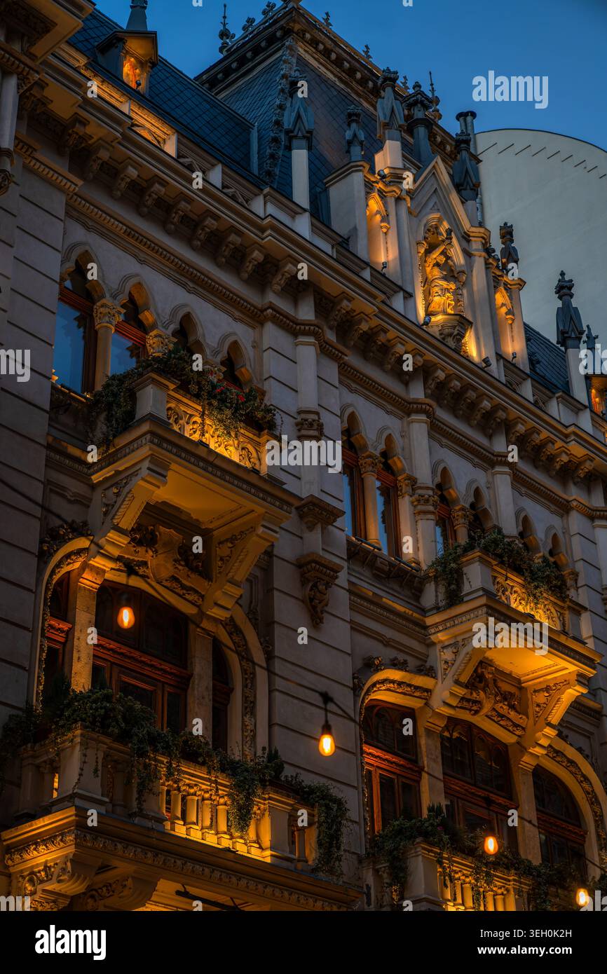 Facciata ornata di un edificio storico con balconi illuminati ed elementi decorativi al crepuscolo a Bucarest, Romania Foto Stock