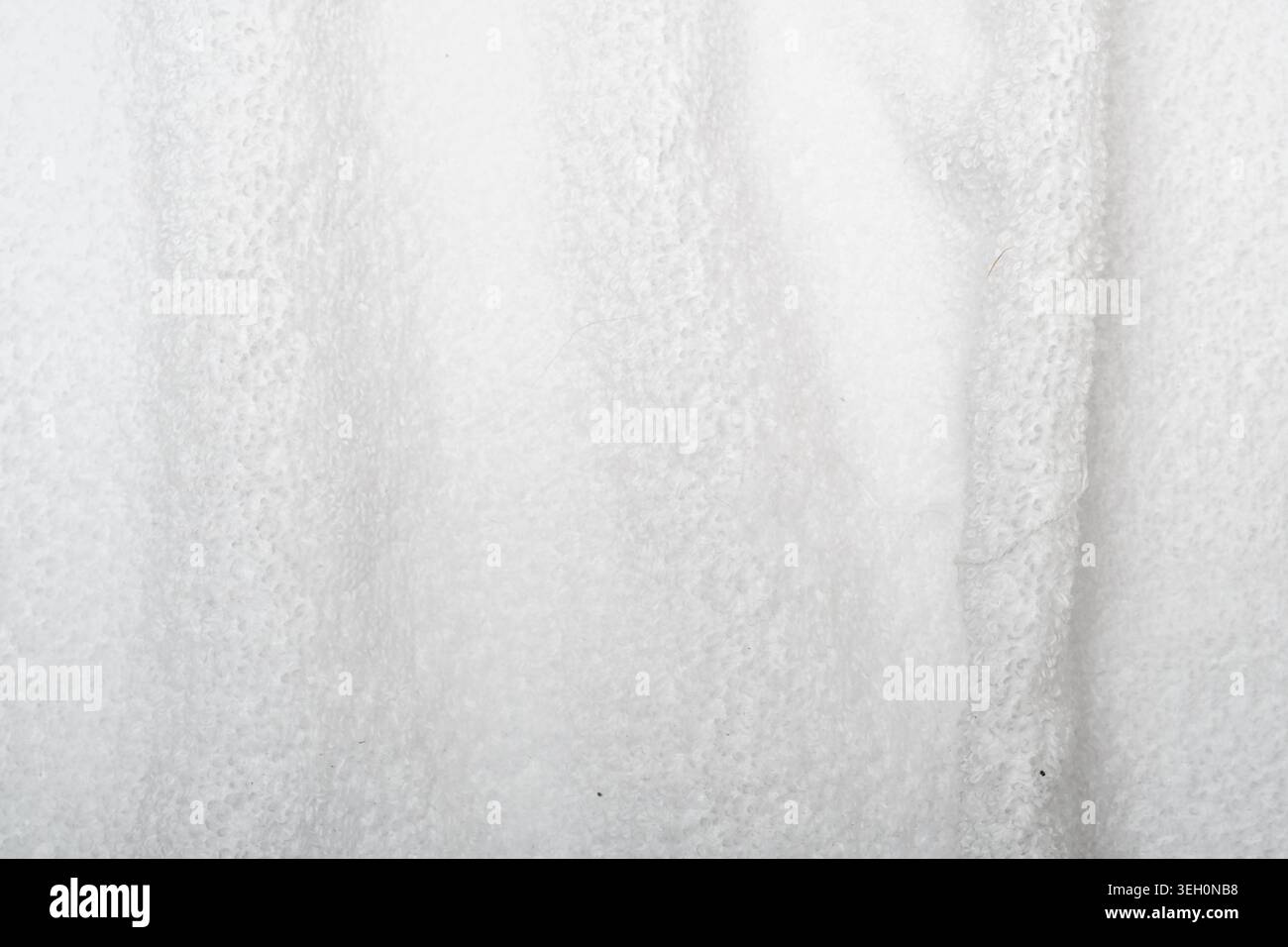 Primo piano di un panno di spugna bianco con pieghe morbide, fibre di cotone visibili e una texture tessile pulita per l'igiene o per la casa. Foto Stock