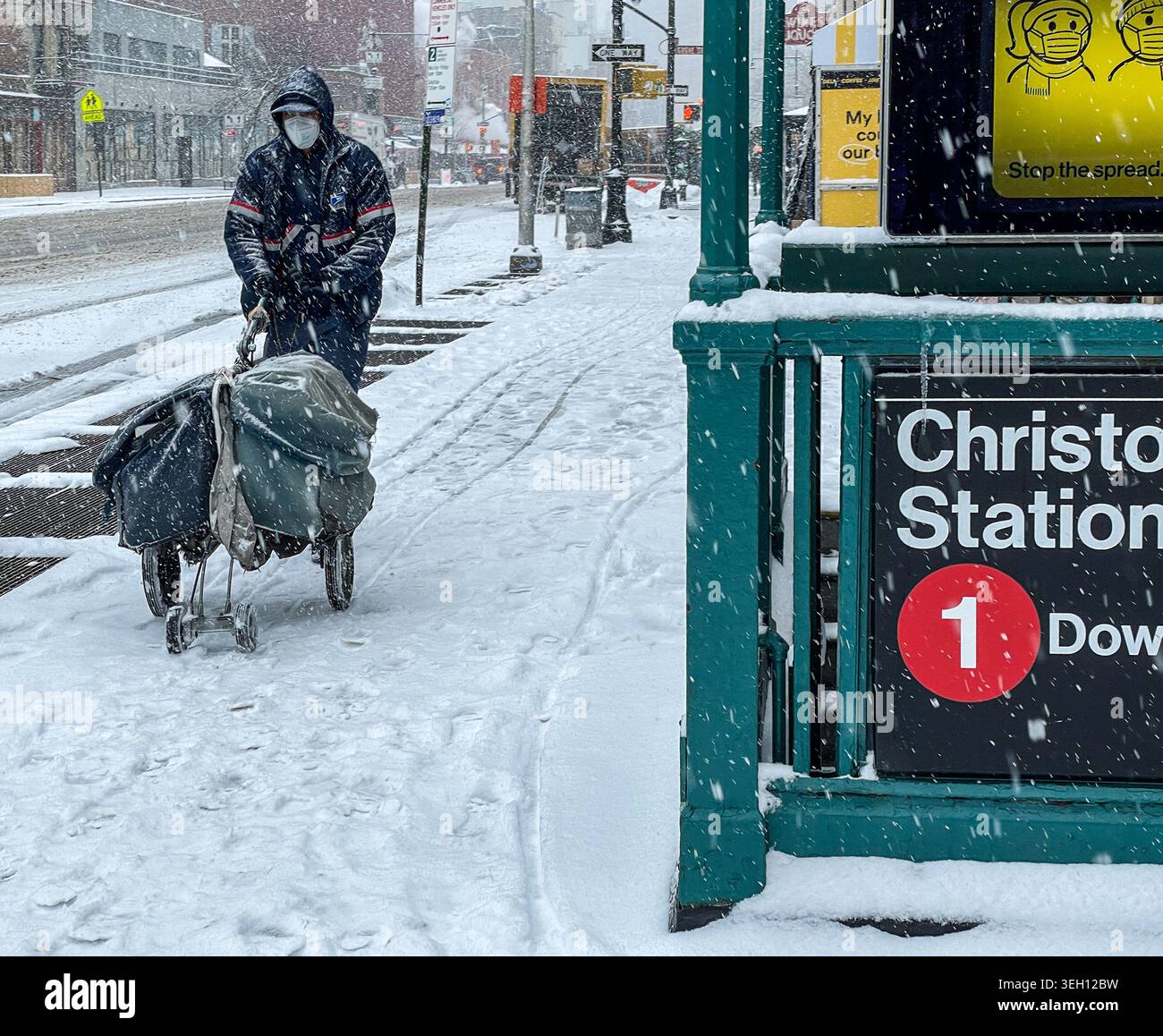 New York, Stati Uniti - 14 maggio 2026: Vista di un impiegato postale che spinge un carrello postale attraverso la neve pesante oltre l'ingresso della metropolitana della Christopher St Station Foto Stock