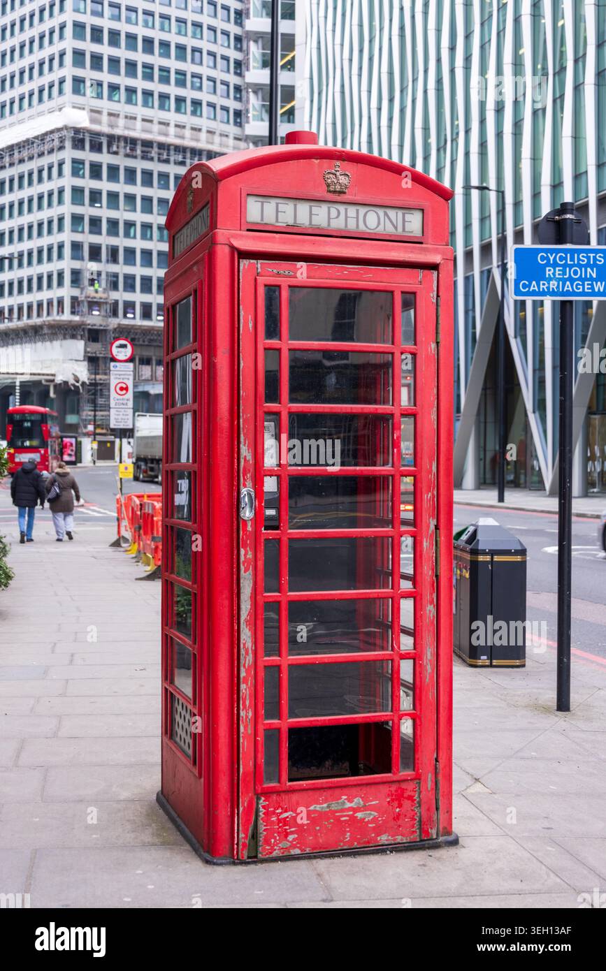 Londra, Regno Unito - 12 maggio 2025: Vista di una classica cabina telefonica rossa su un marciapiede della città con architettura moderna e pedoni nel backgroun Foto Stock