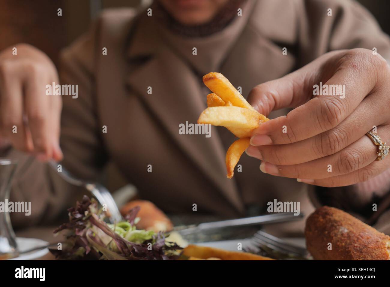 Le mani tengono le patatine fritte a un tavolo durante un pasto con insalata Foto Stock