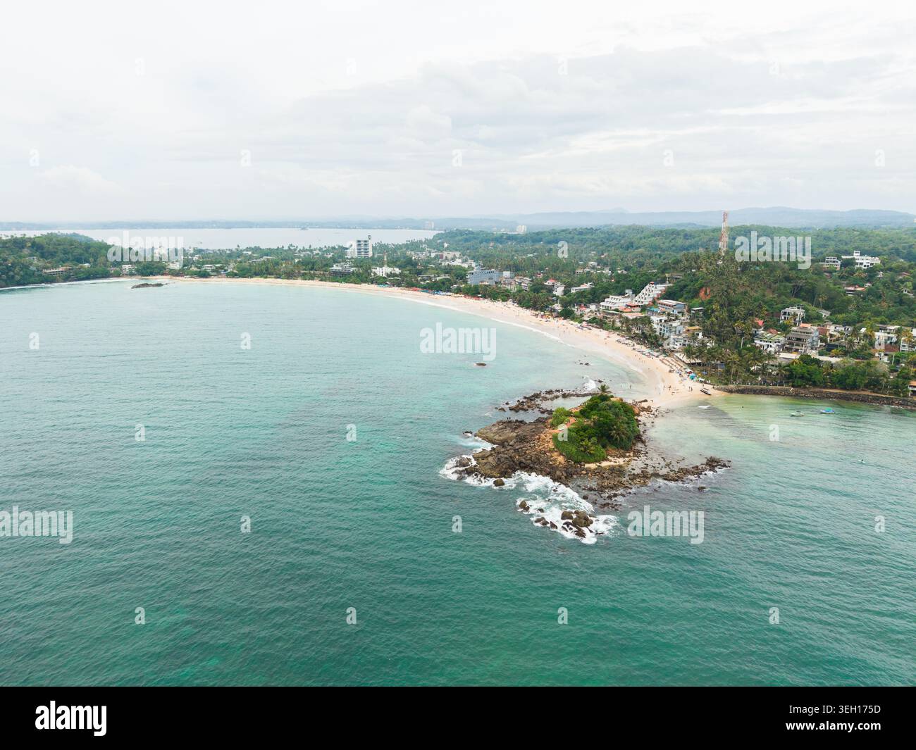 Vista aerea della spiaggia di Mirissa a forma di mezzaluna e della roccia del pappagallo circondati da acque turchesi e da una lussureggiante vegetazione tropicale a Mirissa, Southern Prov Foto Stock