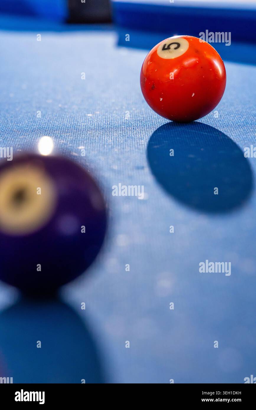 Pallina da biliardo numerata 5 rossa posizionata a destra su feltro blu, guida, sfocatura della palla viola, spazio copia Foto Stock