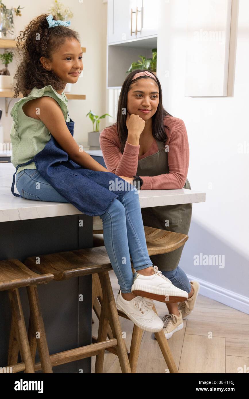 Diverse mamme e preadolescenti afroamericani seduti sull'isola della cucina in grembiuli denim-oliva Foto Stock