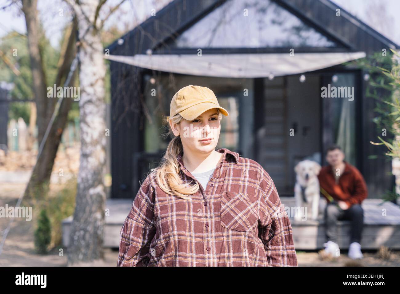 Giovane donna che si prende una pausa tranquilla vicino a una piccola casa moderna durante il ritiro in campagna Foto Stock