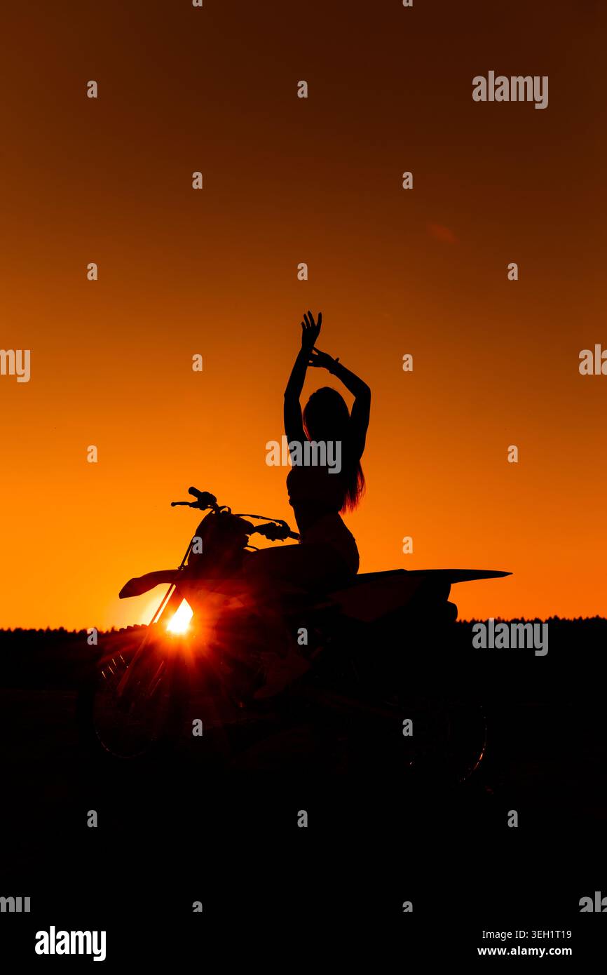 Silhouette femminile seduta su Motocross Bike al tramonto Foto Stock