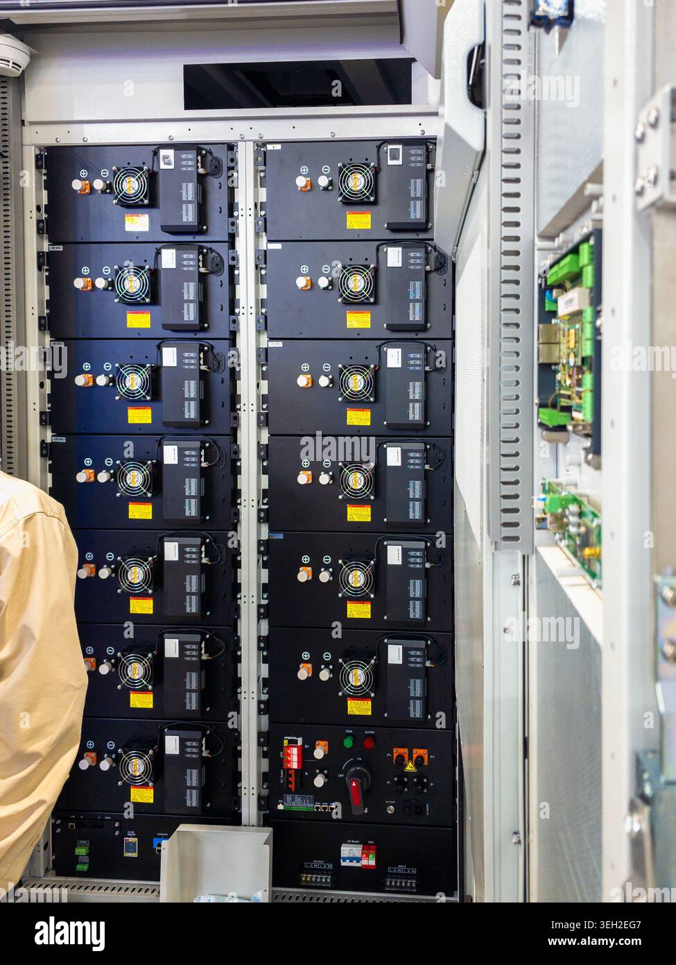 Una vista verticale dei moduli di stoccaggio professionali per batterie al litio impilati in un armadio industriale, con ventole di raffreddamento e collegamenti elettrici. Foto Stock