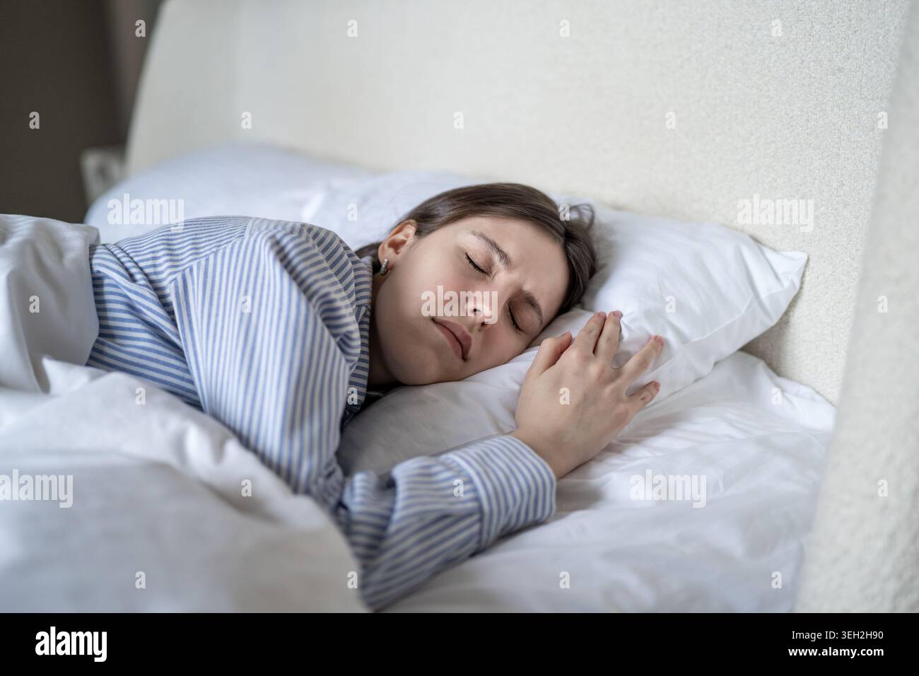 Una giovane donna stanca sdraiata a letto con gli occhi chiusi, sente tensione prima di svegliarsi. Stress mattutino, stanchezza, mancanza di motivazione, insonnia. strug femmina Foto Stock