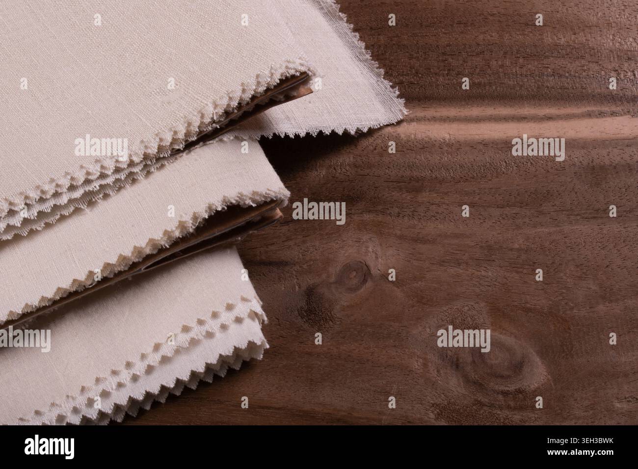Primo piano di campioni di tessuto di seta matka naturale impilato con bordi ruvidi grezzi visualizzati su sfondo in legno. Foto Stock