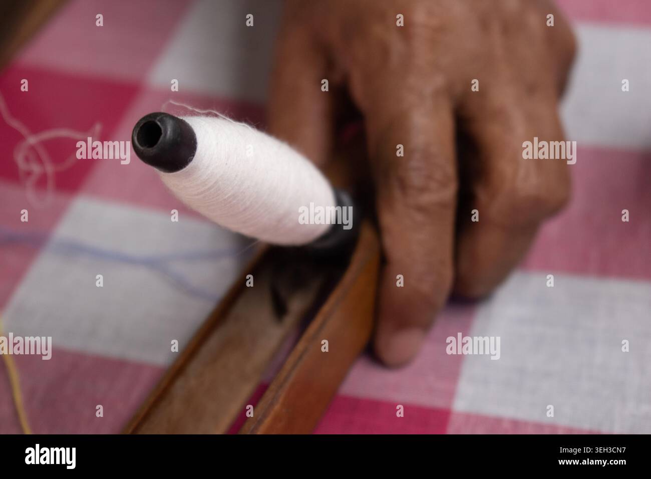 Primo piano di un pirn caricato all'interno di una navetta di legno durante la tradizionale tessitura dei tessuti Jamdani rosa e bianchi su un telaio a mano in India. Foto Stock