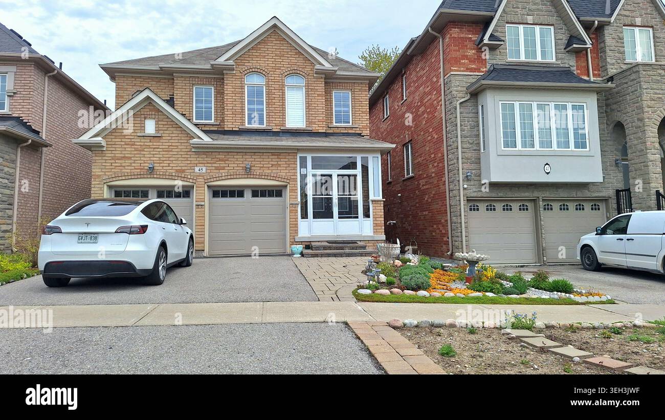 Toronto, ON, Canada - 17 maggio 2026: La strada suburbana presenta case moderne con facciate in mattoni e auto parcheggiate nei vialetti. Foto Stock