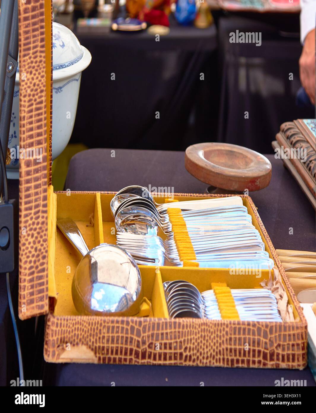 Set di argenteria vintage allestito in una cassa di pelle marrone, che mostra vari utensili tra cui cucchiai e forchette presso un tavolo del mercato delle pulci Foto Stock