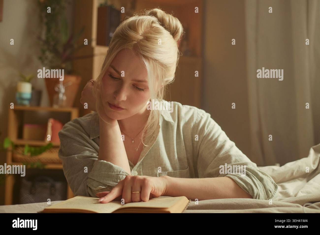 Giovane donna caucasica che legge un libro mentre riposa a letto, studia da sola a casa e riflette tranquillamente. Adatto per campagne di educazione, autoapprendimento, alfabetizzazione, stile di vita Foto Stock