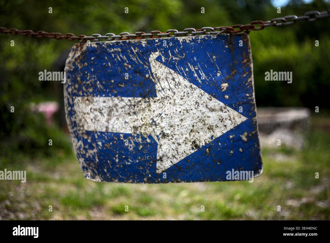 Cartello metallico blu intemprato con una freccia direzionale bianca appesa a una catena arrugginita su uno sfondo in pietra. Foto Stock