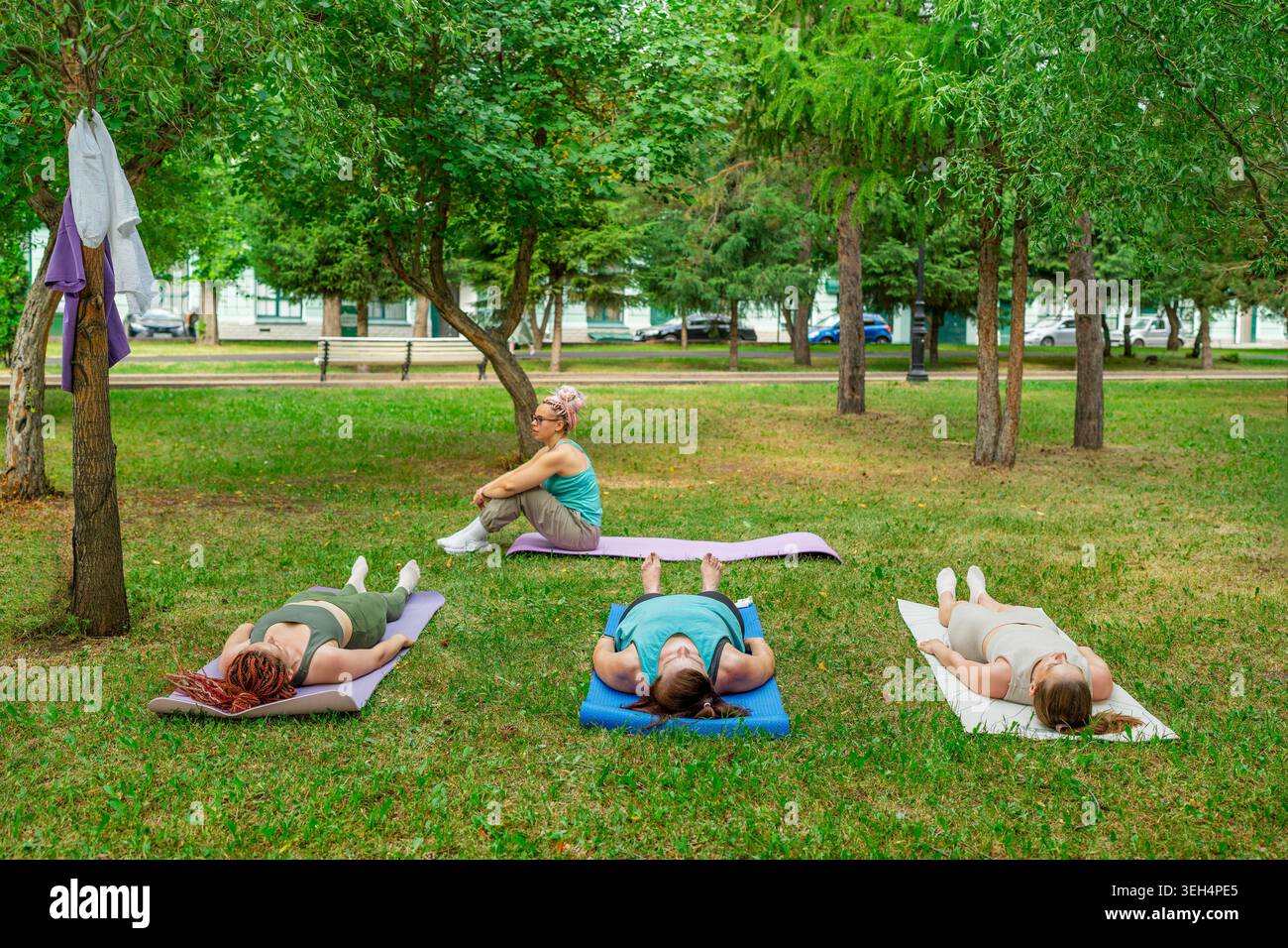 Allenatore di fitness e gruppo di donne sdraiate sui materassini che fanno esercizi di yoga rilassanti nel tranquillo parco verde. Relax, yoga, tappetini, coach, donne, parcheggio. Foto Stock