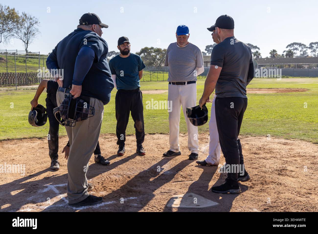 Gruppo di sei uomini, uno anziano, in piedi a casa con cappello da baseball che regge caschi e maschera Foto Stock
