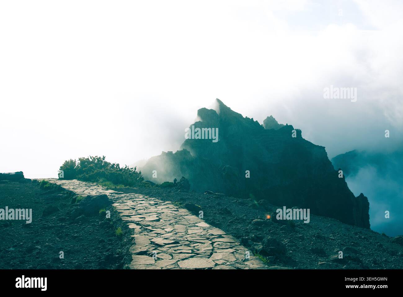 Una spettacolare foto ad alto contrasto di un sentiero lastricato di pietra che attraversa un paesaggio vulcanico roccioso scuro. Il percorso conduce l'occhio direttamente verso un ma Foto Stock