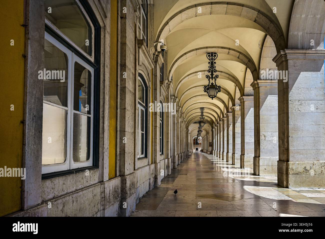Una galleria di pietra splendidamente illuminata con archi ripetuti e lanterne sospese a Lisbona, Portogallo. Foto Stock