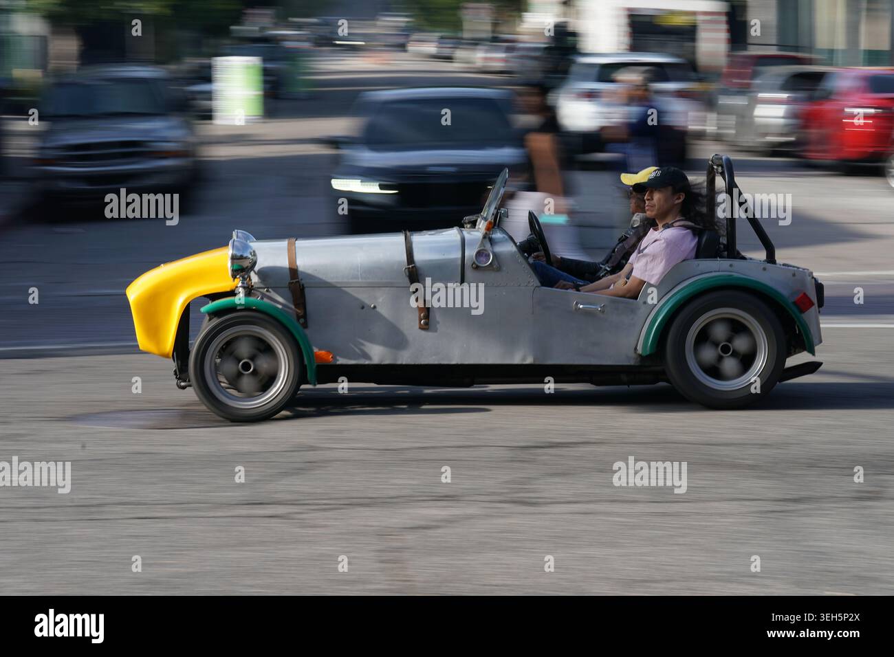 Un'auto personalizzata color argento con un naso giallo percorre una strada trafficata con traffico di fondo sfocato in un movimento di panoramica. Foto Stock