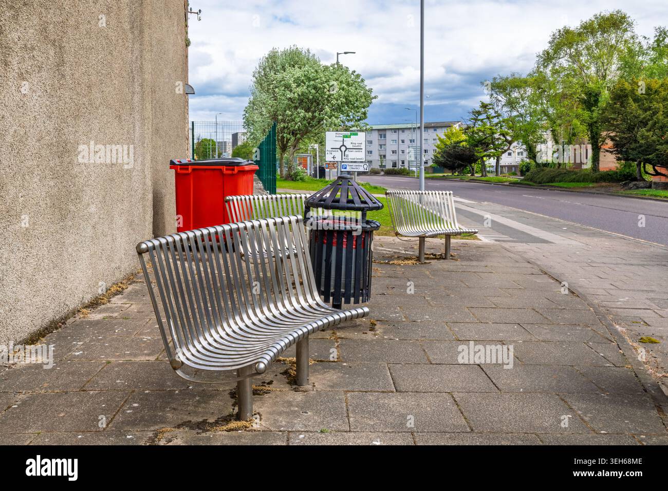 Posti a sedere pubblici, panche e cestino accanto a un marciapiede in un ambiente urbano, che illustra i mobili di strada, gli spazi comuni e la zona pedonale Foto Stock