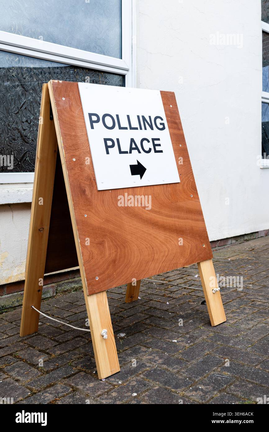 Vista angolata del cartello di un luogo elettorale accanto al muro e alla finestra di un edificio, che rappresenta l'accesso degli elettori, le elezioni e il processo democratico in un ambiente locale Foto Stock