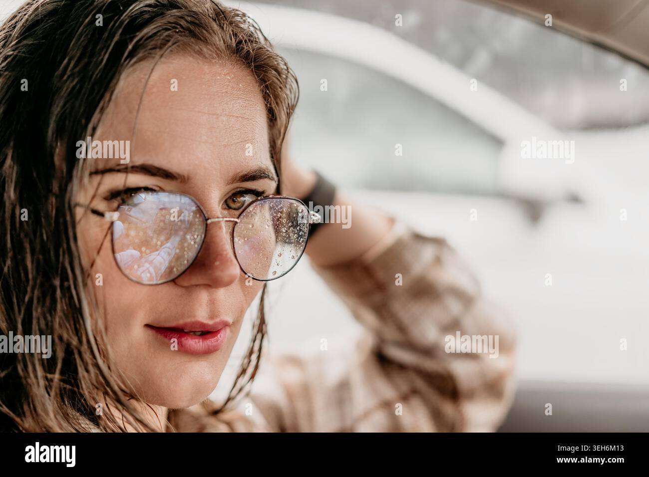 Occhiali da donna gocce di pioggia primo piano ritratto di una giovane donna con i capelli bagnati e gocce di pioggia sugli occhiali all'interno di un'auto Foto Stock